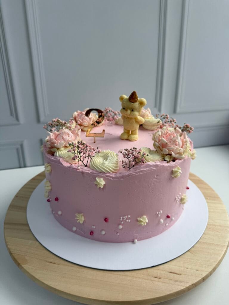 Jednoposchodová krémová torta pre deti na narodeniny v ružovom prevedení zdobená kvetmi a figúrkou.