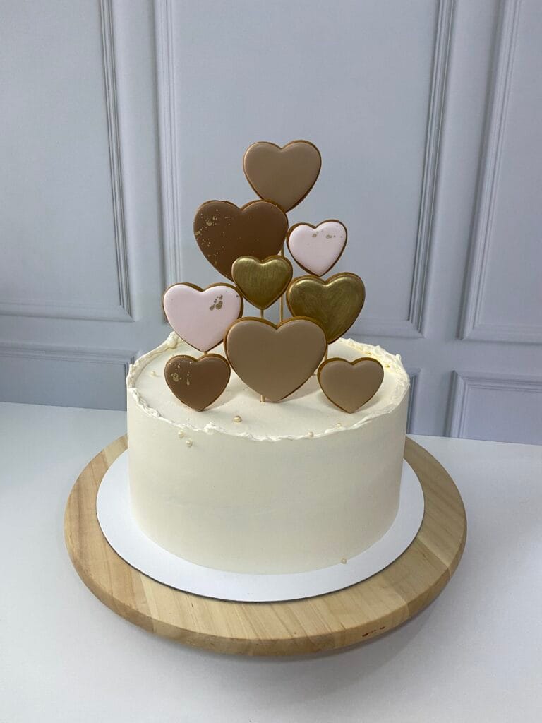 Elegantná jednoposchodová krémová torta zdobená perníkovými srdiečkami.