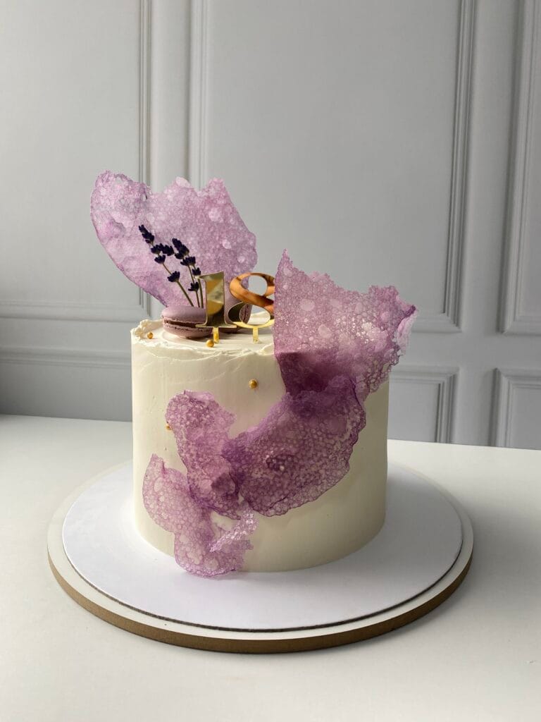 Elegantná jednoposchodová krémová narodeninová torta zdobená kvetmi a makrónkami.